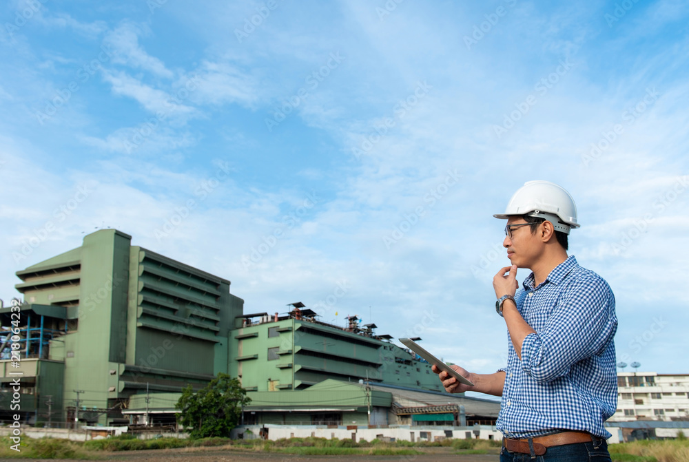Engineer wear white hard hat holding tablet mobile looks green factory, young male engineer using digital tablet outside industry Engineer wear white hard hat holding tablet mobile looks green factory, young male engineer using digital tablet outside industry