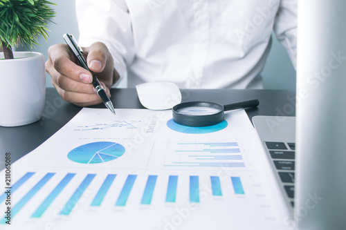 Businessmen use a magnifying glass to analyze the company's data and statistics from the chart.