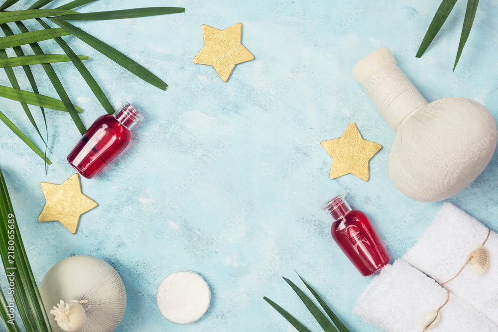 tropical spa mockup: white towels, red shampoo bottles, Thai masage bags, golden stars and green fern leaves on blue background. Text space tropical spa mockup: white towels, red shampoo bottles, Thai masage bags, golden stars and green fern leaves on blue background. Text space