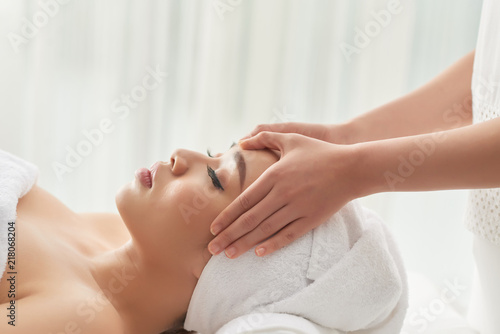 Crop hands of massage therapist rubbing carefully forehead of beautiful lady during spa session in salon © DragonImages