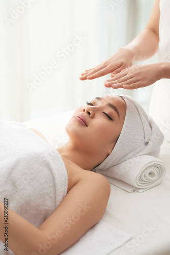 Crop massage therapist holding hands over face of attractive woman during spa session in nice salon