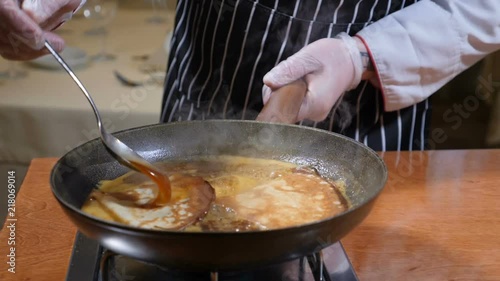 Restaurant cooking concept. Pancakes in boiling caramel sauce. Close up of chef stirring sauce with a spoon. Slow motion photo