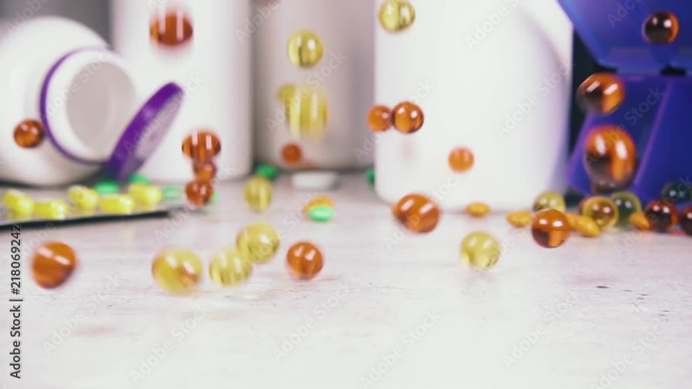 Slow motion yellow and orange capsules with fish oil fall on the table with tablets and plastic bottles Slow motion yellow and orange capsules with fish oil fall on the table with tablets and plastic bottles