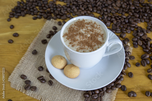Café caliente con canela y galletas con granos de café tostados en el fondo de madera