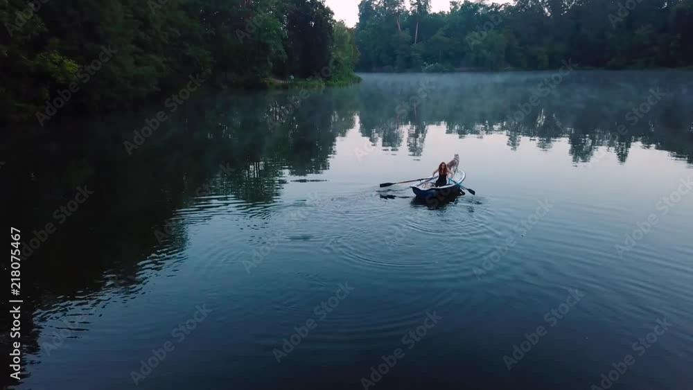 aerial view of young readhead female traveler in the boat on the lake with two siberian husky dogs aerial view of young readhead female traveler in the boat on the lake with two siberian husky dogs
