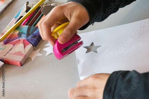 Creative workshop for kids. Drawing on white paper at school. Glue, colorful pencils, star and christmas tree shaped paper cutter on table. Making decorations. Concept of art, crafts, kids having fun.