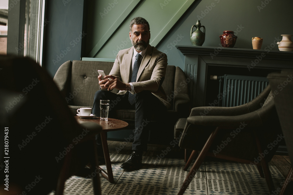 Handsome senior businessman drinking coffee and using mobile phone in lobby Handsome senior businessman drinking coffee and using mobile phone in lobby