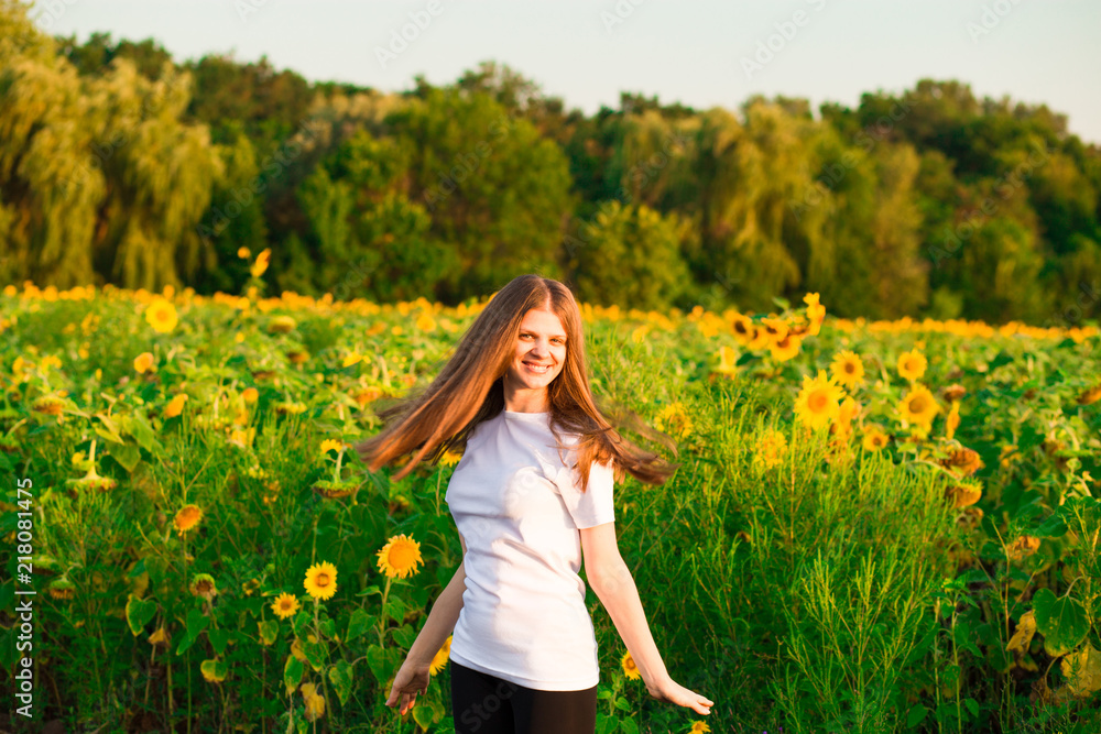 Fototapeta premium Young woman with long hair in sunflower Field with hands up. Beauty girl outdoors enjoying nature