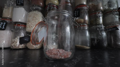 Himalayan rose pink salt pouring into Kilner clip top jar infant of wall of ingredients. photo