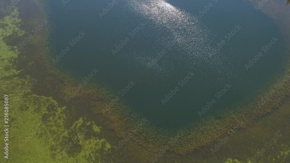 Flying over lake as the sun shimmers on the surface of the water moving past boat towards forest on the shoreline. Flying over lake as the sun shimmers on the surface of the water moving past boat towards forest on the shoreline.