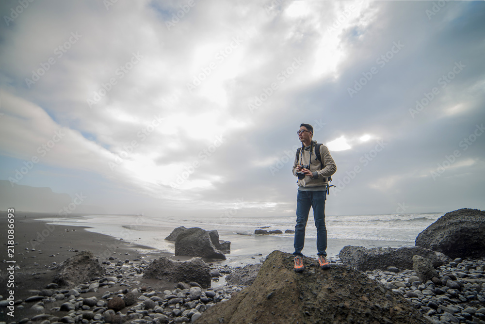 Fototapeta premium Man traveler stood on the rock to enjoy the view at Black sand beach, Vik. Iceland