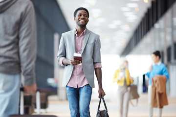 Cheerful African-American man standing with passport in hall of airport