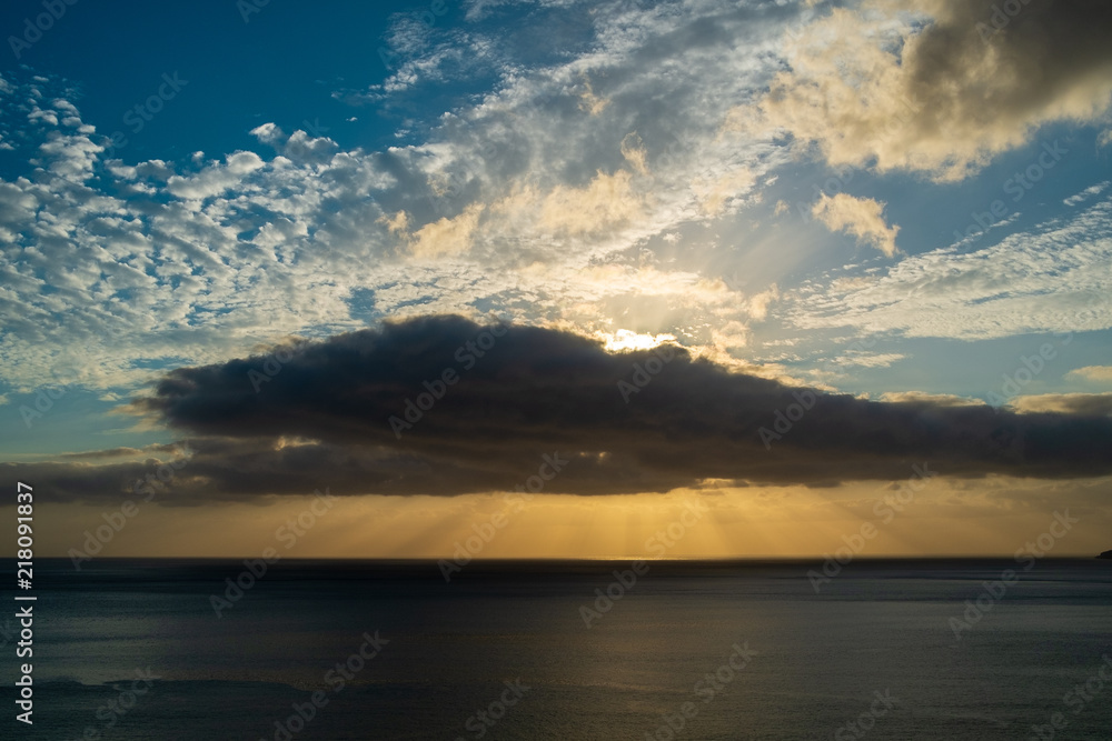Sunset behind some clouds over the sea with orange and blue sky Sunset behind some clouds over the sea with orange and blue sky