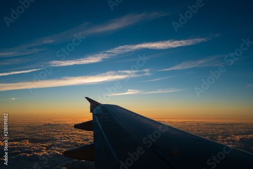 Sunset trough the window of an air plane and a wing with some clouds