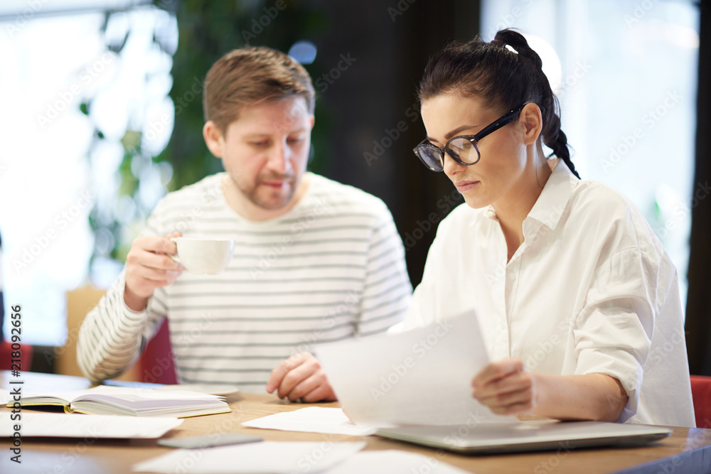 Stylish adult woman and man working with papers in team sitting at desk in light office Stylish adult woman and man working with papers in team sitting at desk in light office