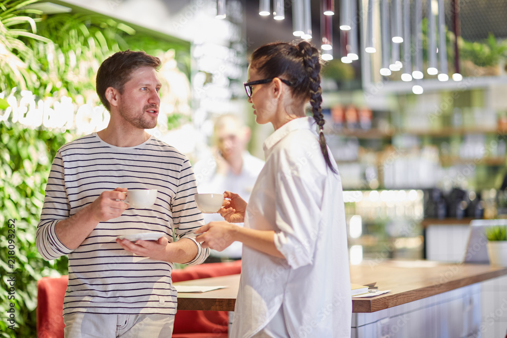 Naklejka premium Trendy woman and man standing in modern cafeteria and talking in relaxation while having coffee