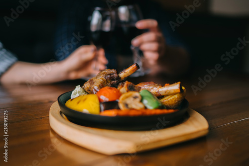 Glasses of red wine with food on table. Selective focus, blurred couple toasting with glasses of red wine in the restoran. Blurred abstract background of clinking glasses of wine. Selective focus.