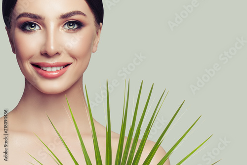Attractive spa woman model with healthy skin, cute smile and green palm leaf. Facial treatment, cosmetology and spa beauty