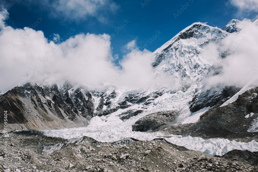 High mountains with snowy peaks in clouds at bright sunny day in Nepal. Colorful landscape with beautiful rocks and dramatic cloudy sky. Nature background. Amazing mountains. Way to Everest base camp.
