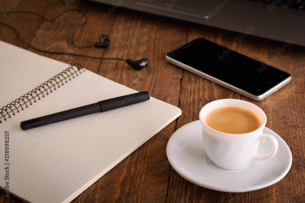 Cup of coffee on a laptop keyboard. Work place modern. Laptop (notebook) with cup of coffee and notepad with pen on old wooden table. Cup of coffee on a laptop keyboard. Work place modern. Laptop (notebook) with cup of coffee and notepad with pen on old wooden table.