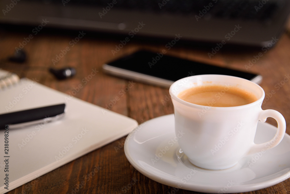 Cup of coffee on a laptop keyboard. Work place modern. Laptop (notebook) with cup of coffee and notepad with pen on old wooden table. Cup of coffee on a laptop keyboard. Work place modern. Laptop (notebook) with cup of coffee and notepad with pen on old wooden table.