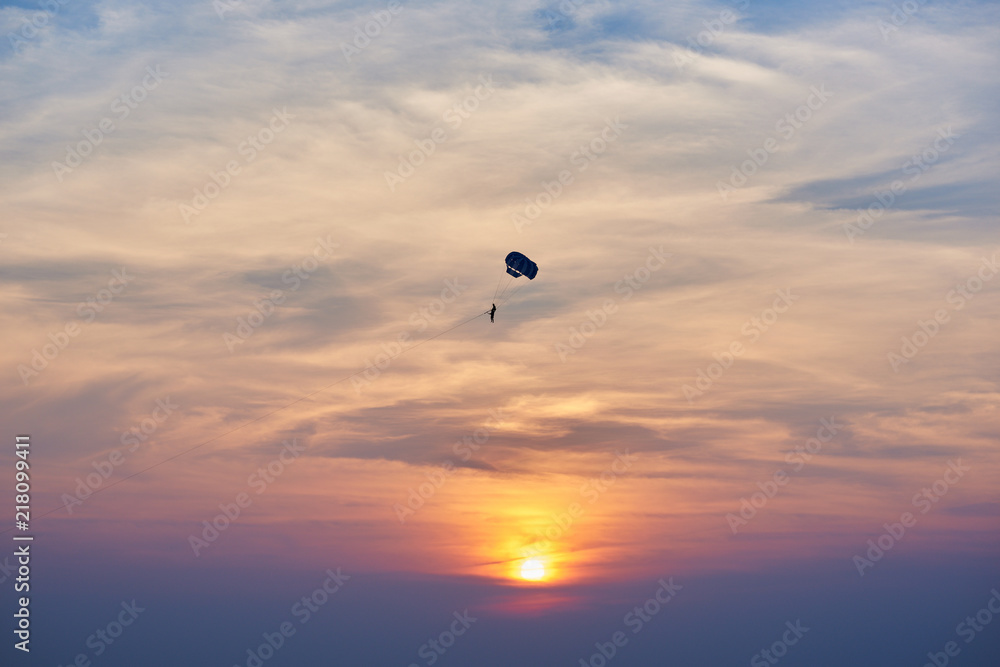 Sunset over the ocean. Silhouette of a lonely parachute on sunset background. Sky, clouds and water. Beautiful serene scene. Natural composition of nature. Landscape. Concept of outdoor activities.