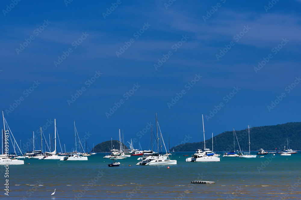 View of many beautiful moored  yachts parking and floating on calm blue sea in a sunny weather, modern water transport, summertime vacation, luxury lifestyle and wealth concept. Tropical landscape.