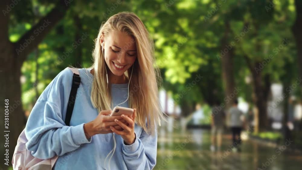 Happy blonde lady in headphones smiling and using smartphone while listening music in the street
Happy blonde lady in headphones smiling and using smartphone while listening music in the street