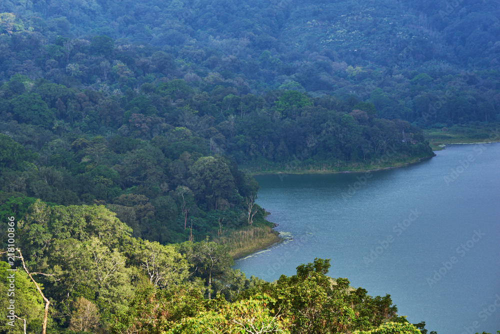 Forested mountain slope in low lying cloud with the evergreen tropical trees, shrouded in mist in a scenic landscape. Low cloud shrouds the distant mountains above the waters of the lake.