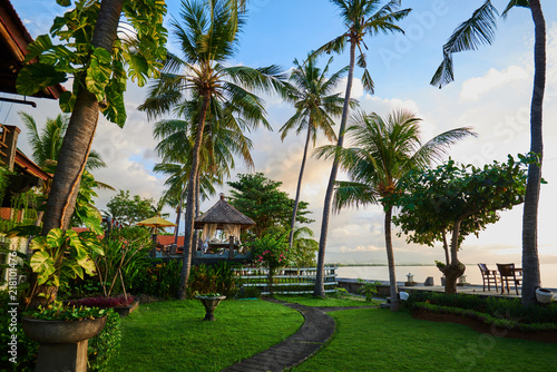 Beautiful view on the tropical bungalow in the green garden with palms and flowers. Asian beach resort. Exotic landscaping design. Stone footpath to paradise beach. Vacation and travel concept.
