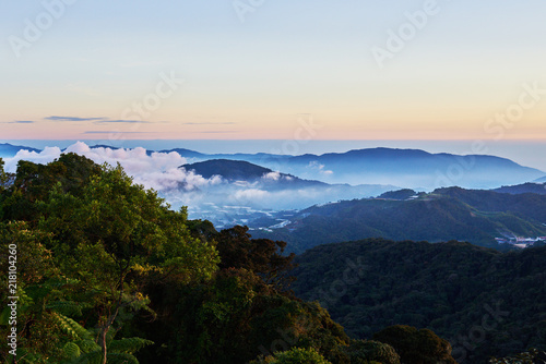 Mountain hill covered with forest on foreground and curly clouds on background with foggy valley with village in between. Mountains during sunrise. Beautiful natural landscape in the summer time.. © eskstock