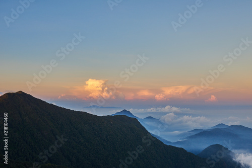 Hills in valley between the mountains with fog and curly clouds illuminated by the rising sun.