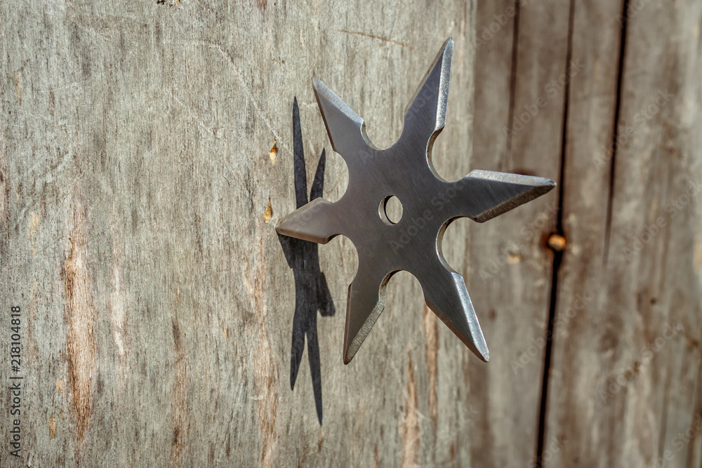 Shuriken (throwing star), traditional japanese ninja cold weapon stuck in wooden background Shuriken (throwing star), traditional japanese ninja cold weapon stuck in wooden background