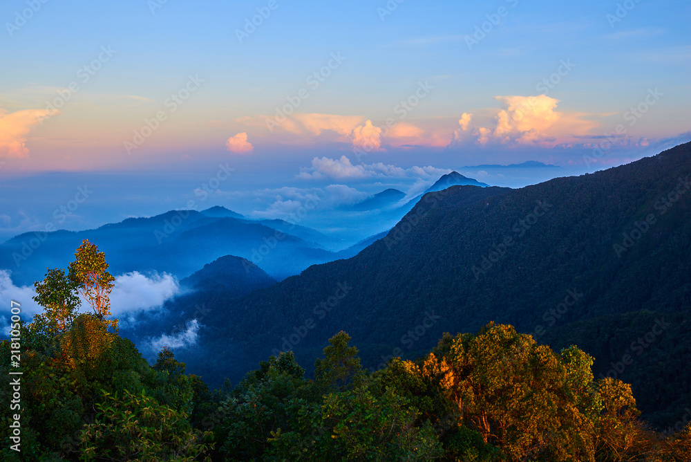 Obraz premium Mountains during sunset. Beautiful natural landscape in the summer time. A multicolored mist covered the hills. Low clouds between the peaks shrouding the most distant. Travel and adventure concept.