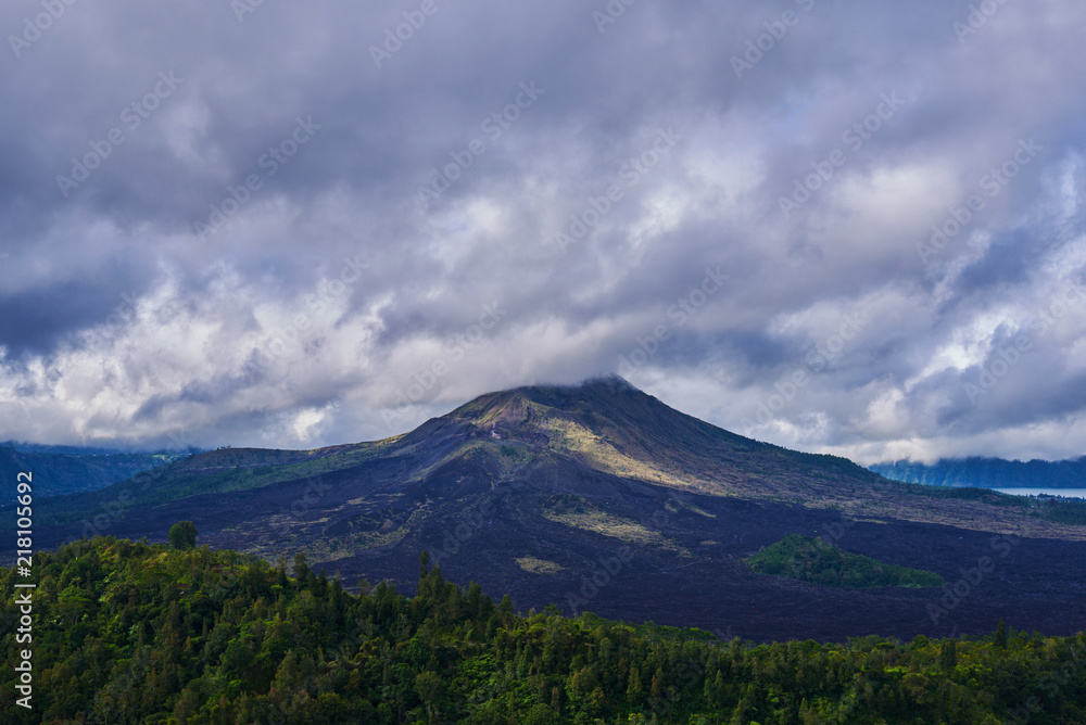 Travel background. Rural sunrise landscape. Countryside and green tropical forest. Natural background. Landscape of Batur volcano on Bali island, Indonesia. Dramatic sky with clouds in the mountains.