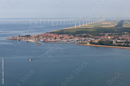 Aerial view Dutch fishing village with harbor and big offshore wind turbines along the coast