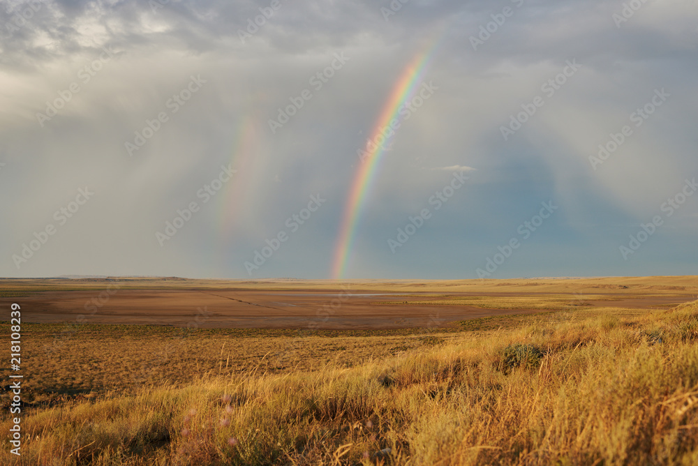 Rainbow in sky among  landscape over the boundless savannah, summer nature background, blue sky with clouds. The rainbow crosses the sky over desert. The concept of exotic tourism.