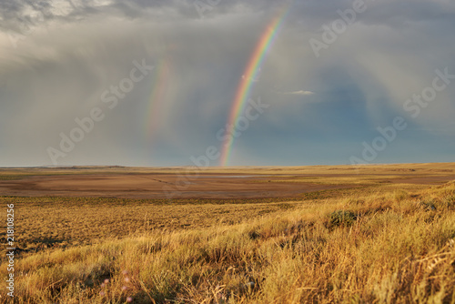 Rainbow in sky among landscape over the boundless savannah, summer nature background, blue sky with clouds. The rainbow crosses the sky over desert. The concept of exotic tourism.