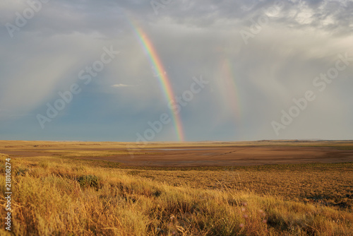 Rainbow in sky among landscape over the boundless savannah, summer nature background, blue sky with clouds. The rainbow crosses the sky over desert. The concept of exotic tourism.