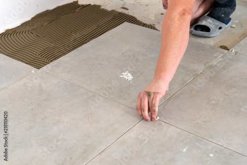 A tiler's hand is putting a spacer between a ceramic tiles.