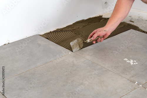 The hands of the tiler are laying the ceramic tile on the floor.