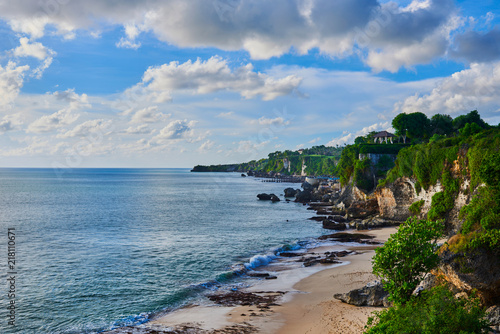 Scenic landscape. Panorama of the rocky tropical coast, cliffs and stones, green forest and houses on the shore, against a background of large cumulus clouds. Coastline of South Kuta, Bali, Indonesia