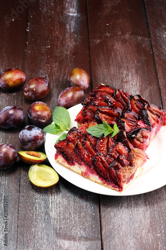 Rustic plum cake on wooden background with plums around.