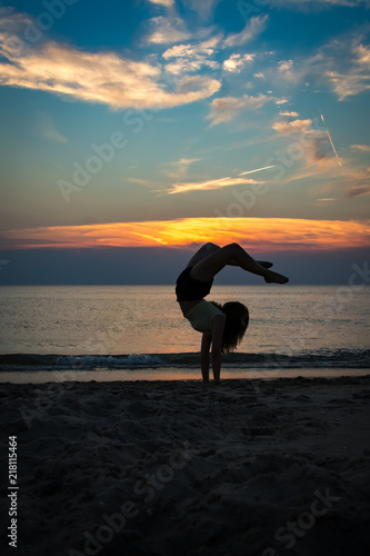 junge Ballerina vollzieht Handstand am Strand mit Meer und einem perfekten Sonnenuntergang im Hintergrund