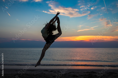 junge Ballerina vollzieht einen Sprung am Strand mit Meer und einem perfekten Sonnenuntergang im Hintergrund