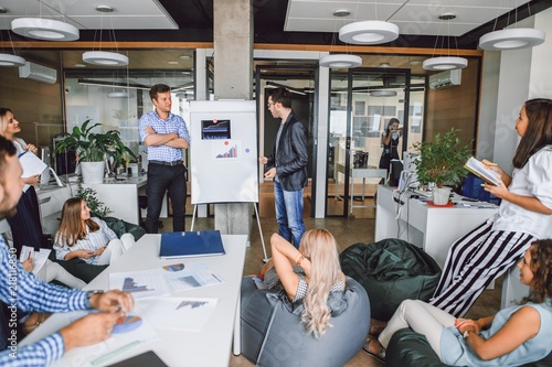 Corporate meeting of creative entrepreneurs in the office, two men speak to colleagues