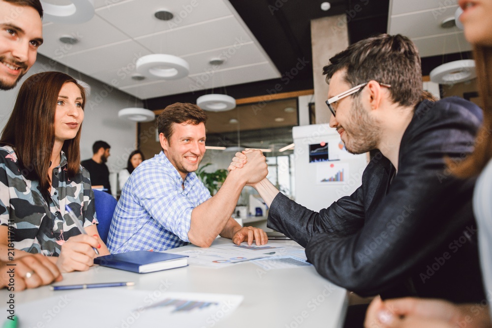 Creative business people compete at the table in the office with the help of arm wrestling Creative business people compete at the table in the office with the help of arm wrestling