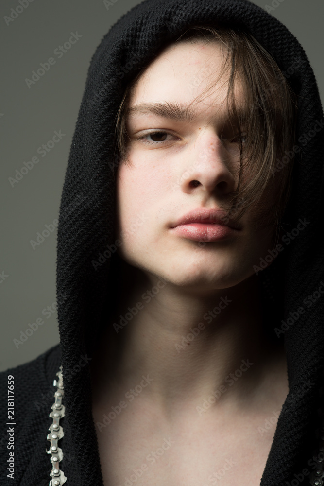 Fototapeta premium Macho in black bathrobe with hood, close up. Guy on confident face in black hood, grey background. Masculinity concept. Man with smooth skin on face and neck looking at camera.