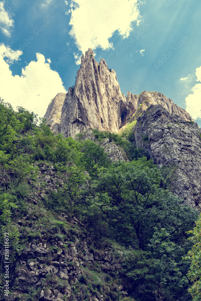 High mountain peak and forest against blue sky with clouds in Turda gorge, Romania