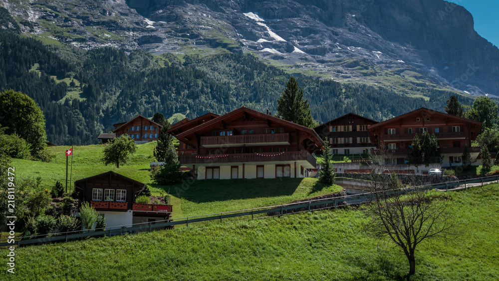 Traditional wooden chalets in picturesque Swiss town Grindelwald in summer in front of the north face of the Eiger mountain surrounded by vibrant green pastures